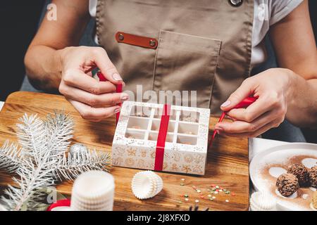 Woman Chocolatier verpackt Schokolade in Schachteln. Hochwertige handgefertigte Schokoladentrüffel. Süßes Geschenk zu Weihnachten oder Neujahr. Nahaufnahme der weiblichen Hände und t Stockfoto