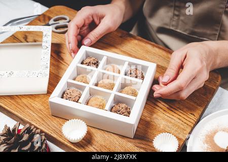 Hochwertige handgefertigte Schokoladentrüffel. Die Schokoladenfrau verpackt Schokolade in Schachteln. Nahaufnahme von weiblichen Händen und leckeren Süßigkeiten. Stockfoto