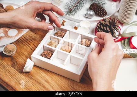 Hochwertige handgefertigte Schokoladentrüffel. Die Schokoladenfrau verpackt Schokolade in Schachteln. Nahaufnahme von weiblichen Händen und leckeren Süßigkeiten. Weibliche Hände. Stockfoto