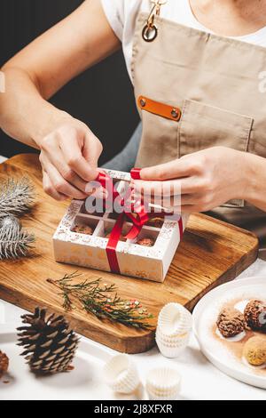 Woman Chocolatier verpackt Schokolade in Schachteln. Hochwertige handgefertigte Schokoladentrüffel. Nahaufnahme von leckeren Süßigkeiten. Vertikale Aufnahme Stockfoto