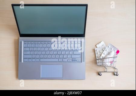 Online-Apotheke Konzept. Draufsicht auf einen Laptop und einen Einkaufswagen voller Medikamente auf dem Desktop. Pillen im Internet mit Lieferung nach Hause kaufen. Stockfoto