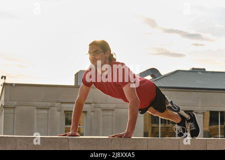 Ein Mann mit einer Behinderung macht Liegestütze, während er im Freien trainiert. Stockfoto