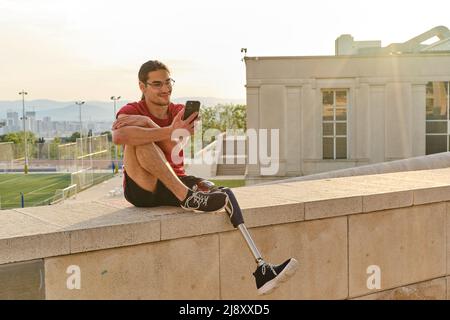 Mann mit einer Behinderung, der sein Smartphone benutzt, während er im Freien sitzt. Stockfoto