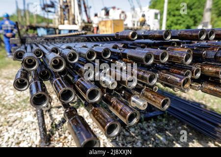 Bohrrohre für Ölbohranlagen, die im Hintergrund mit Mitarbeitern der Ölindustrie gestapelt sind. Öl- und Gasindustrie. Ölpumpe Wagenheber auf einem Ölfeld. Bohren von Öl und Stockfoto