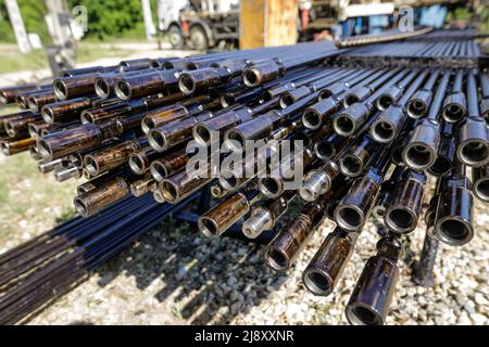 Bohrrohre für Ölbohranlagen, die im Hintergrund mit Mitarbeitern der Ölindustrie gestapelt sind. Öl- und Gasindustrie. Ölpumpe Wagenheber auf einem Ölfeld. Bohren von Öl und Stockfoto