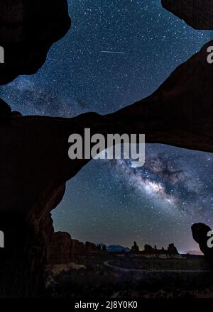 Ein Metero schländelt über den Mily Way, während er den ikonischen Double Arch im Arches National Park in der Nähe von Moab, Utah, durchstreift. Stockfoto