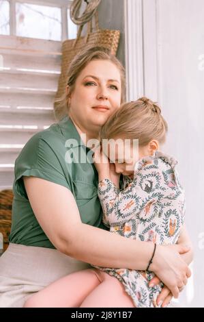 Glückliche Familie Mutter mit kleinen Kind Tochter Mädchen haben Spaß in Vorort Land Hausleben an sonnigen Tag. Ehrliche Mutter hält Kind in Armen und Knien und Stockfoto