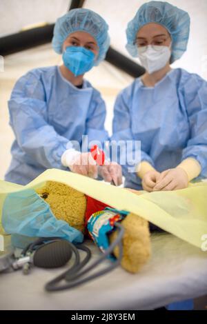 17. Mai 2022, Sachsen-Anhalt, Magdeburg: Die Medizinstudenten Bibi (l) und Vanessa vom Universitätsklinikum Magdeburg operieren in der Teddyklinik einen Teddy, der spielerisch Magenschmerzen hat. Die Teddy-Klinik wird von Medizinstudenten des Universitätsklinikums Magdeburg betrieben und hatte am Morgen vor dem Schlafsaal des Universitätsklinikums eröffnet. Rund 620 Kinder sind registriert und können sich dort spielerisch ihre Kuscheltiere untersuchen lassen. Am Freitagnachmittag gibt es eine offene Sprechstunde, in der Kinder ihre Teddybären auch ohne Vorregi untersuchen lassen können Stockfoto