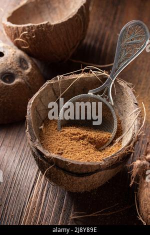 Kokos-brauner Zucker in einer Kokosnuss-Schale auf einem Holzhintergrund Stockfoto