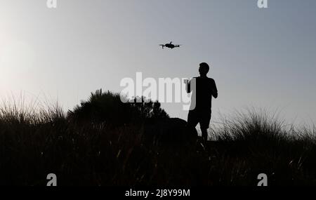 Pollenca, Spanien. 18.. Mai 2022. Ein Mann lässt seine Drohne neben Cap de Formentor in der Serra de Tramuntana fliegen, dem nördlichsten Teil der Insel Mallorca und einem der touristischsten Orte. Viele Orte auf der Insel sind für ihre wunderschönen Sonnenuntergänge und Aussichten geschätzt. Quelle: Clara Margais/dpa/Alamy Live News Stockfoto