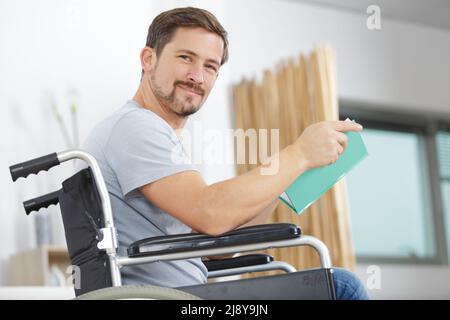 Körperlich behinderter Mann im Rollstuhl mit Buch Stockfoto