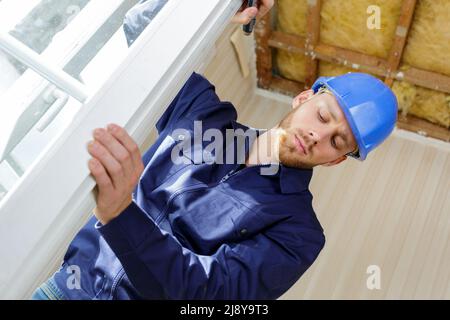 Bauarbeiter, der im Haus ein Schaumstoffband auf das Fenster legt Stockfoto