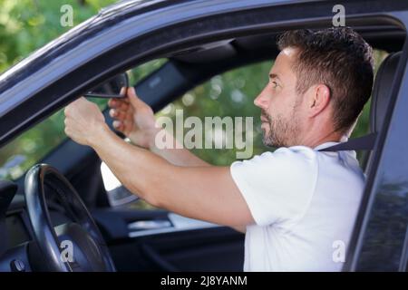 Mann, der den Spiegel im Auto justiert Stockfoto