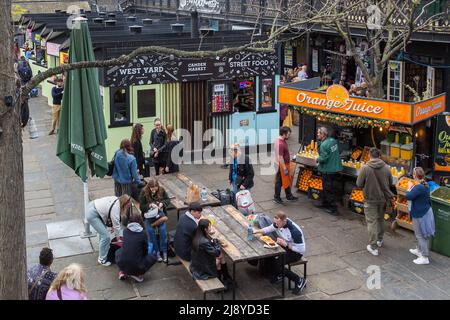 Im West Yard auf dem Camden Market, inmitten der Fülle von Lebensmittelhändlern, sitzen Menschen draußen, um zu essen. Stockfoto