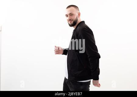 Lächelnd, selbstbewusst Brunet Mann schauen Kamera, posieren gehen Spaziergang im Studio auf weißem Hintergrund. Halten Sie etwas in der Hand Stockfoto