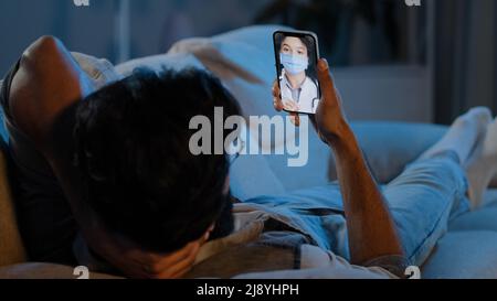 Unkenntlich krank krank Mann liegt auf der Couch zu Hause in der Nacht in der Dunkelheit Gefühl unwohl online Beratung Video Anruf an Frau Arzt dringende Hilfe r Stockfoto