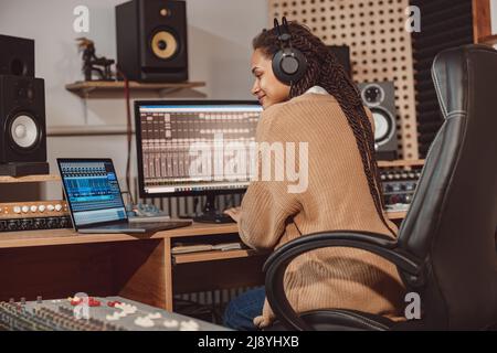 Afrikanische nette Bloggerin nimmt Online-Podcast mit Laptop, Kopfhörer und Mikrofon in professionellen Musikstudio Stockfoto