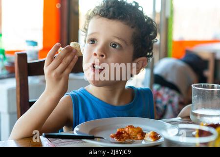 Lockiger kaukasischer Junge, der im Restaurant isst Stockfoto