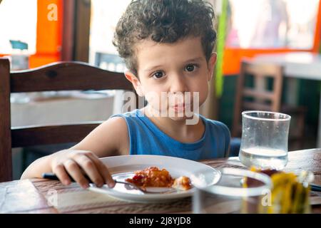 Schöner kaukasischer Junge mit lockigen Haaren, der im Restaurant isst Stockfoto