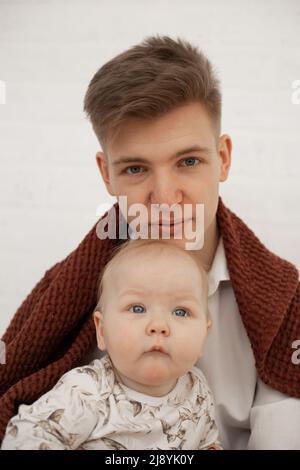 Porträt von jungen müde Vater Vater Vater bedeckt mit braunen Plaid hält kleine niedliche plump grauäugigen Baby Kleinkind Kleinkind. Stockfoto