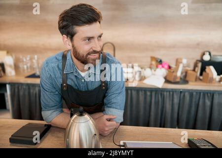 Lächelnder Barista, der mit dem Kunden spricht, während er hinter einem Tresen steht Stockfoto