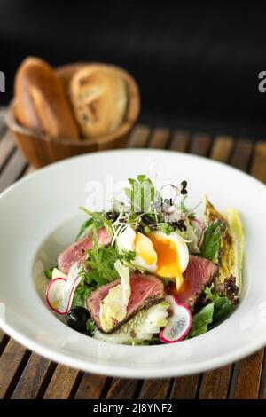 nicoise-Salat mit frisch gebratenen Thunfisch und gekochtem Ei auf dem Holztisch Stockfoto