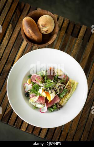 nicoise-Salat mit frisch gebratenen Thunfisch und gekochtem Ei auf dem Holztisch Stockfoto