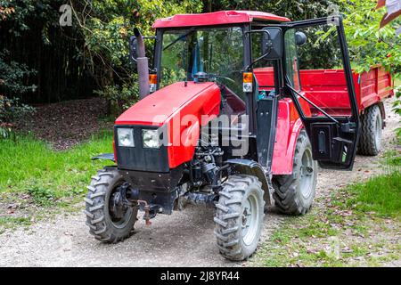 Roter Radtraktor mit Anhänger auf einer unbefestigten Straße in einem Laubwald Stockfoto