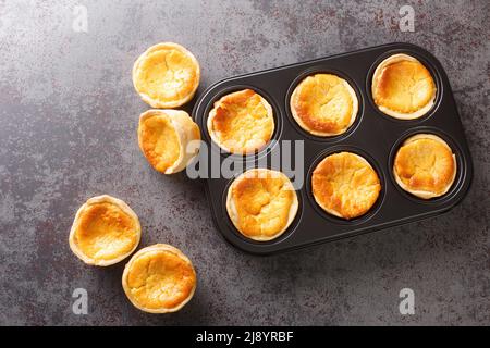 Queijadas oder Queijadinhas, kleine portugiesische Käsekuchen, die mit Queijo Fresko aus der Nähe in einer Backform auf dem Tisch zubereitet werden. Horizontale Draufsicht von oben Stockfoto