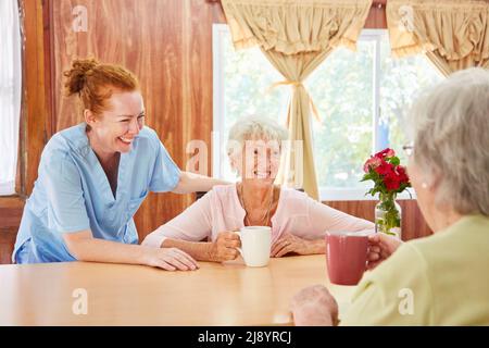 Senioren sitzen zusammen und trinken Kaffee im Pflegeheim und unterhalten sich mit einer Krankenschwester Stockfoto