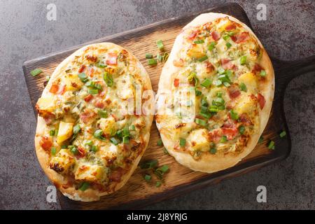 Traditionelle deutsche Pizza mit Käse, Kartoffeln, Zwiebeln und Speck aus der Nähe auf einem Holzbrett auf dem Tisch. Horizontale Draufsicht von oben Stockfoto