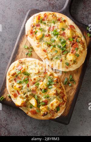 Deutsche Pizza Schwäbische Dinnete mit Kartoffeln, Zwiebeln und Speck aus nächster Nähe auf einem Holzbrett auf dem Tisch. Vertikale Draufsicht von oben Stockfoto