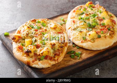 Traditionelle deutsche Pizza mit Käse, Kartoffeln, Zwiebeln und Speck aus der Nähe auf einem Holzbrett auf dem Tisch. Horizontal Stockfoto