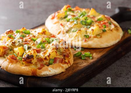 Offener Kuchen mit Käse, Kartoffeln, Zwiebeln und Speck aus der Nähe auf einem Holzbrett auf dem Tisch. Horizontal Stockfoto