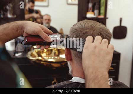 Ein alter Mann, der in einem Friseurladen einen Haarschnitt von einem Meister genießt. Ein alter Mann bekommt einen stylischen Haarschnitt Stockfoto