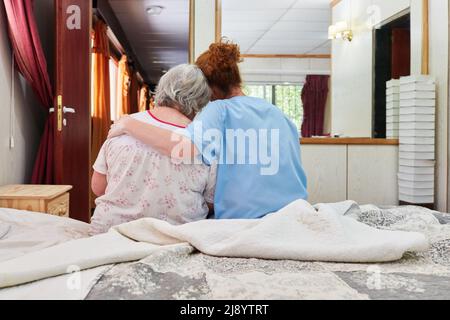 Fürsorgliche geriatrische Krankenschwester umarmt und tröstet kranke ältere Frau im Hospiz oder Pflegeheim Stockfoto