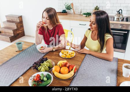 Zwei junge Freundinnen sitzen am Tisch und reden und essen Stockfoto