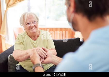 Fürsorgliche geriatrische Krankenschwester hält die Hände der älteren Frau als Komfort im Pflegeheim oder zu Hause Stockfoto