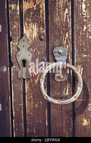 Alte Vintage Doork Nock. Hölzerne alte Tür mit Schlüsselloch und schäbigen Metallgriffen in Form eines Rings. Stockfoto