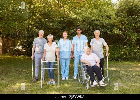 Gruppe von Senioren mit Rollstühlen und Gehhilfen zusammen mit Pflegepersonal im Garten der Rehabilitationsklinik Stockfoto