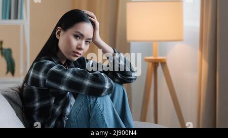 Allein müde Langeweile traurig asiatische Frau erschöpft Mädchen sitzt auf der Couch zu Hause Gefühl unsicher unglücklich Traurigkeit schlecht Gefühl psychische Probleme Psychologie beunruhigend Stockfoto