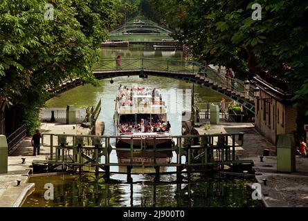 Ein Canauxrama-Boot, das auf dem Kanal Saint-Martin nach Norden fährt und am Pont tournant de la Grange-aux-Belles auf dem Kanal Saint-Martin vorbeifährt. Stockfoto