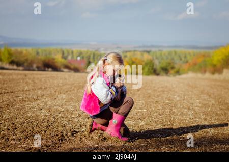 Kleines Kind, das eine Hauskatze hält und allein in sonniger herbstlicher Atmosphäre geht Stockfoto