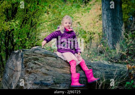 Kleines Kind, das im Baumstamm in einer zauberhaften, farbenfrohen Landschaft sitzt Stockfoto