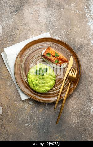 In der Pfanne angebratenes weißes Fischfilet mit Edamamiampuree auf rustikalem Hintergrund Stockfoto