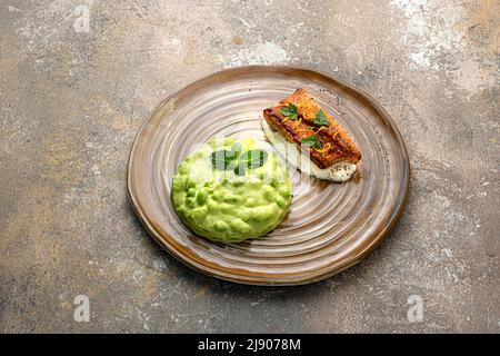 In der Pfanne angebratenes weißes Fischfilet mit Edamamiampuree auf rustikalem Hintergrund Stockfoto