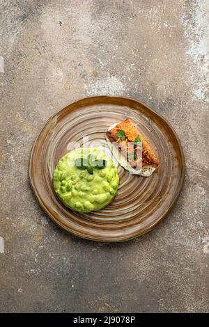 In der Pfanne angebratenes weißes Fischfilet mit Edamamiampuree auf rustikalem Hintergrund Stockfoto