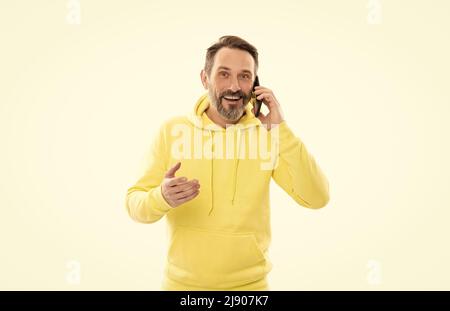 Lächelnder, hübscher, reifer Mann im Kapuzenpulli, der isoliert auf Weiß telefoniert, spricht. Stockfoto