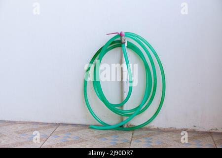 Die Rolle des Gummiwäschers hängt am Wasserhahn in der Nähe der weißen Wand der Garage außerhalb des Stadthauses. Stockfoto