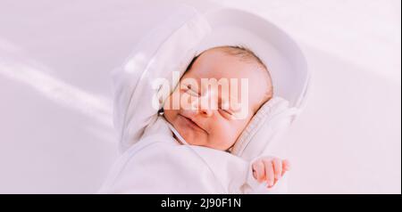 Das Kind trägt Kopfhörer. Frohes Baby. Ein neugeborenes Baby. Weiß auf Weiß Stockfoto